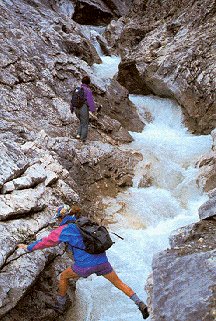 A hiker leaps an icy stream.