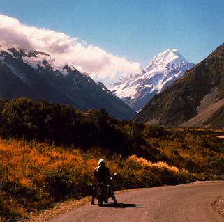 A cyclist pauses to enjoy a snowcapped peak.