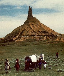 Wagon train beneath the spire of Chimney Rock.